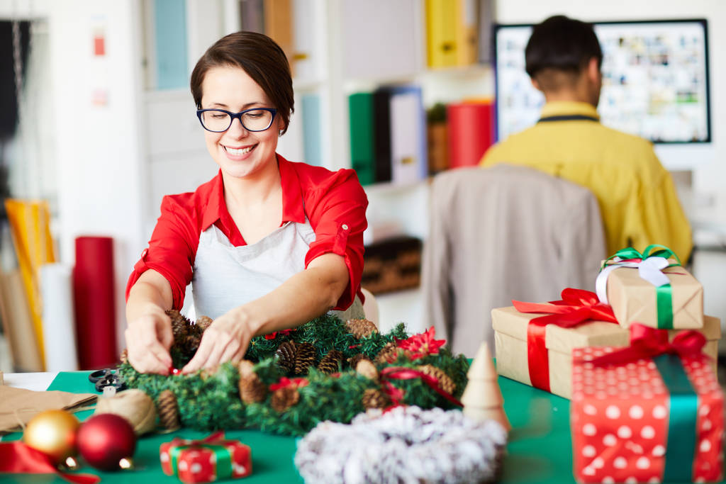 Mulher sentada à mesa mexendo em decoração de Natal e presentes para funcionários