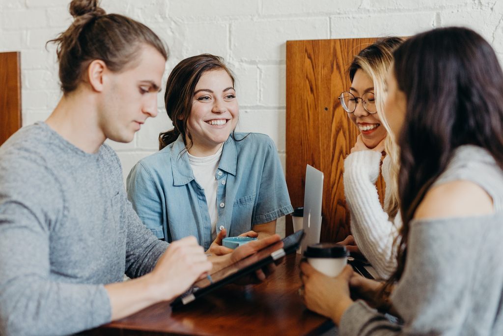 Grupo de quatro pessoas, três sorrindo e um concentrado usando tablet, simbolizando os benefícios e importância do Employer branding