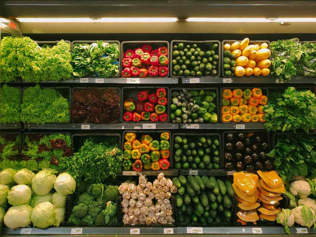 Simbolizando vale cesta básica: Prateleira de supermercado com vários legumes e verduras como alface, pimentão, abóbora, couve-flor, pepino etc todos separados em seções